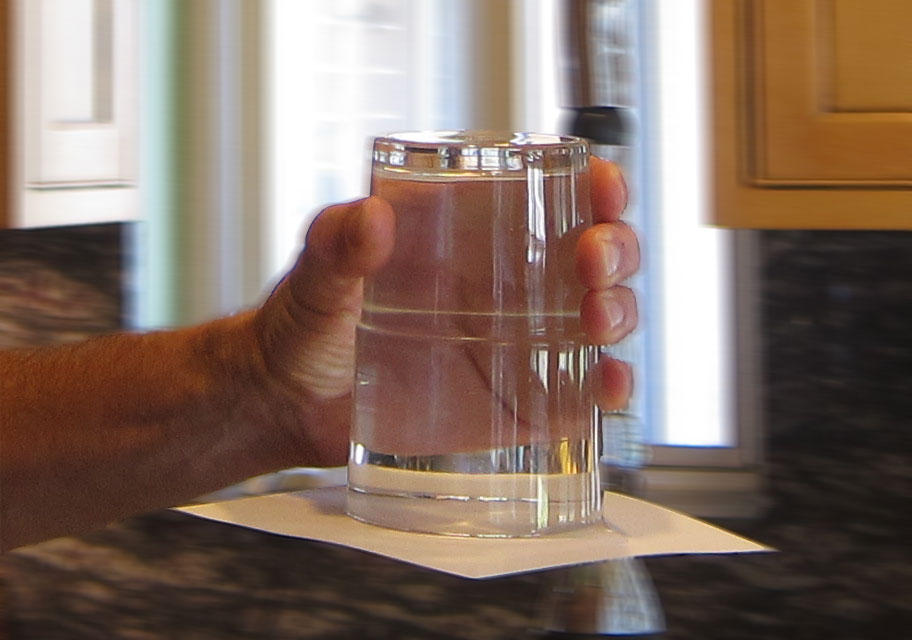 Holding a glass of water upside down with slip of paper on the bottom